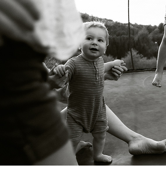 Black and white photo of baby in striped onesie smiling up at mom while standing