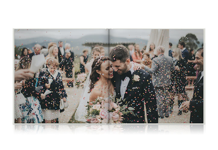 Album photo mariage paysager ouvert avec une photo d'un couple descendant l'allée couverte de confettis.