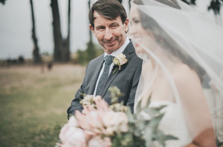 Father smiles and walks bride down the aisle on grassy land