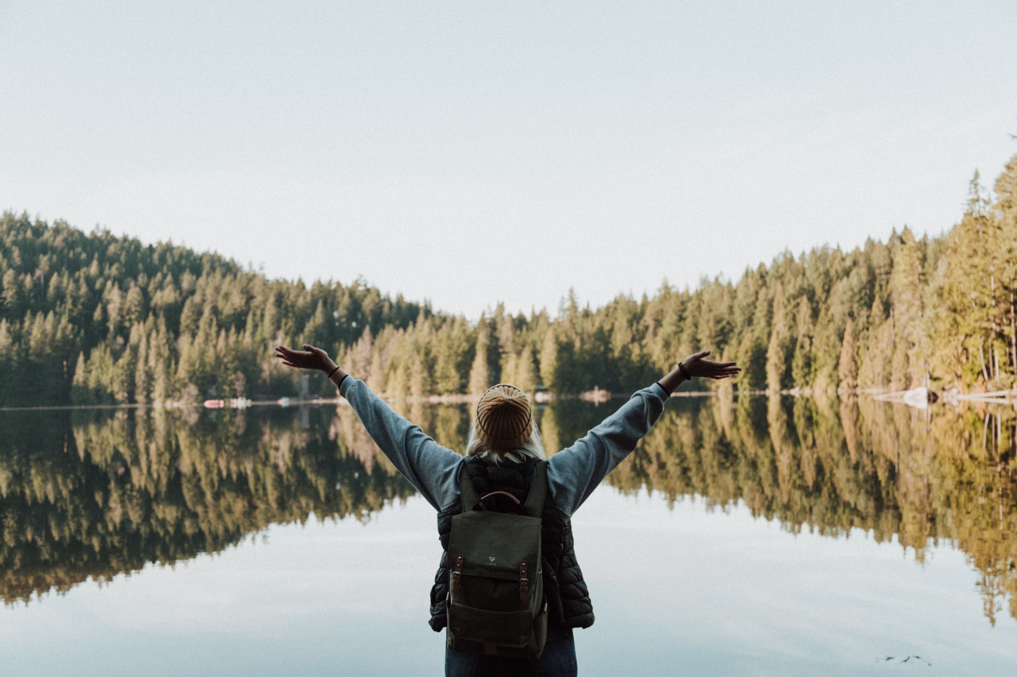 Woman with arms raised looking out at lake and trees