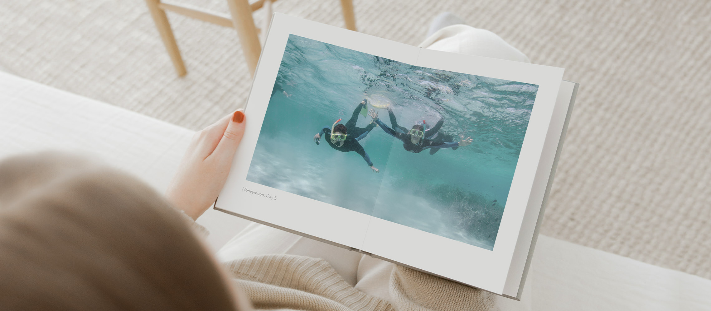 Woman with red nails reads portrait photo book of underwater snorkeling couple on their honeymoon