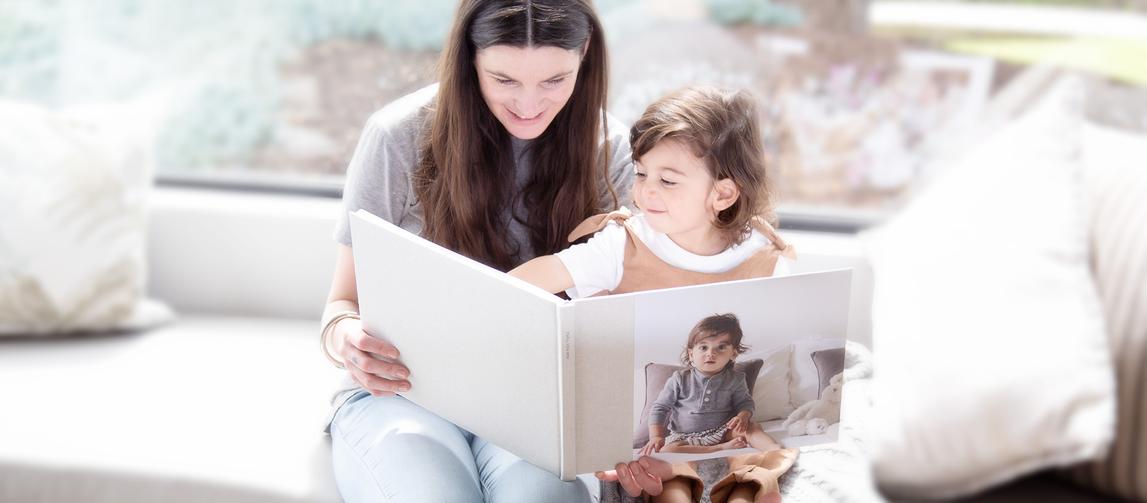 A mãe folheando o álbum de fotos com a filha em um sofá.