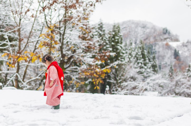 Young toddler girl in pink coat walks through snow in forest